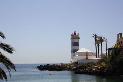 Lighthouse by sea against clear sky