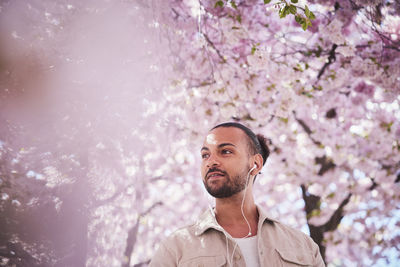 Young man standing under cherry blossom and listening to music