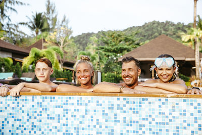 Happy family leaning on poolside in resort during vacation