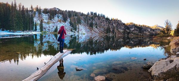 Rear view of woman standing on driftwood in lake during winter