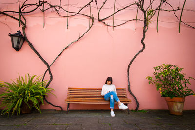 Young woman sitting on bench by wall