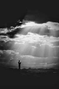 Silhouette man standing on rock against sky