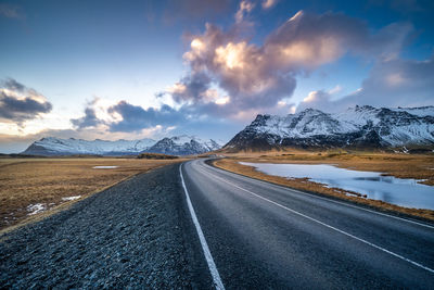 Road amidst snowcapped mountains against sky during winter