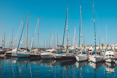 Sailboats moored on harbor against clear blue sky