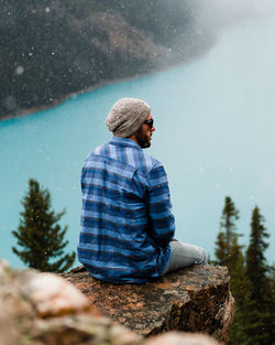 Young man sitting on snow covered tree