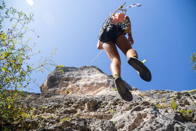 Low angle view of man jumping on rock against sky