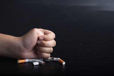 Close-up of hand holding cigarette over black background