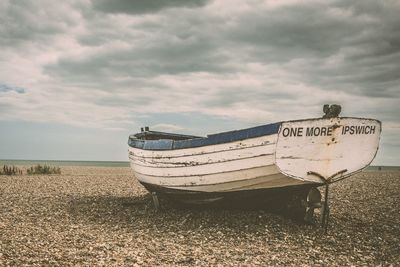 Old boat moored on beach against sky