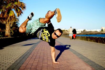 Young man practicing handstand on footpath