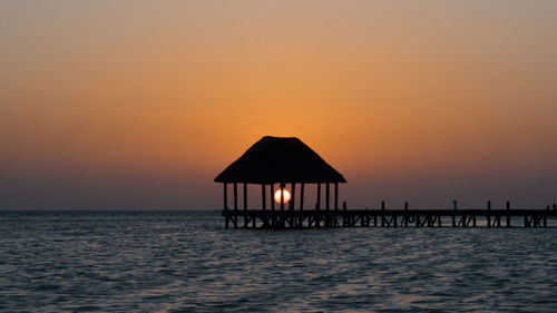 Silhouette built structure on sea against clear sky during sunset