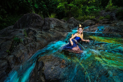 Woman sitting on rock by stream in forest