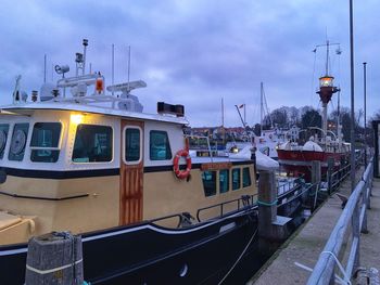 Boats moored on illuminated street against sky at dusk