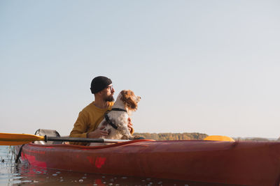 Man with dog sitting in boat against clear sky