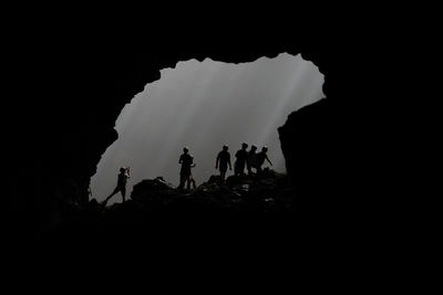 Silhouette people standing on rock formation against sky