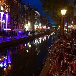 Illuminated street by buildings in city at night