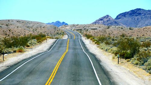 Empty road amidst mountains against clear sky