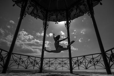 Low angle view of woman jumping in gazebo against sky