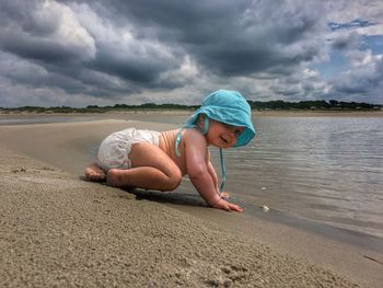 Rear view of woman sitting at beach against sky