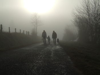 Rear view of men walking on sidewalk in foggy weather