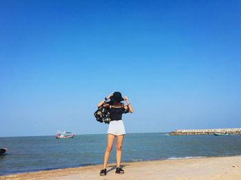 Full length of woman standing at beach against clear blue sky