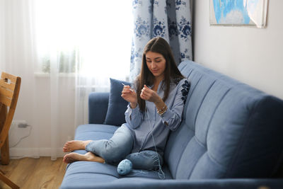 Young woman crocheting  sitting on sofa at home