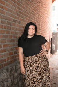 Portrait of smiling young woman standing against brick wall