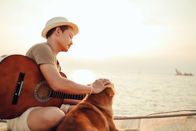 Young woman sitting on guitar at beach against sky