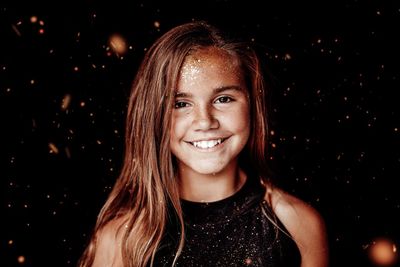 Portrait of smiling girl in glitter against black background