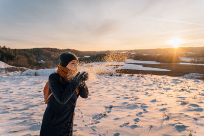 A woman blows snow from her palms on a snow-covered field in winter