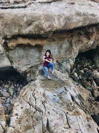 Young woman using mobile phone while sitting on rock