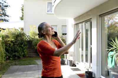 Senior woman talking on mobile phone in front of house