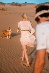 Rear view of woman with dog walking on sand at desert