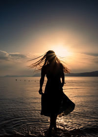 Rear view of woman standing at beach against sky during sunset