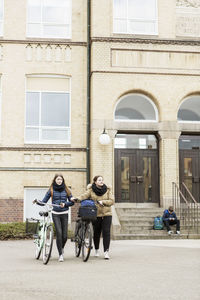 Schoolgirls with bicycles outside school building