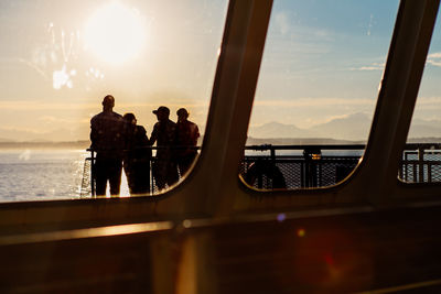 People on glass window against sky during sunset