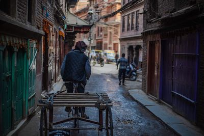 Rear view of young man riding bicycle on street amidst buildings