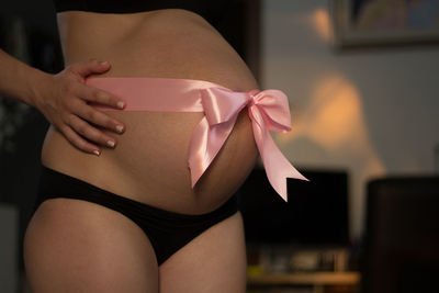 Midsection of pregnant woman with tied bow on her belly at home