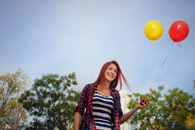 Portrait of smiling woman holding balloons against trees