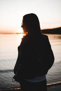 Rear view of woman standing at beach during sunset