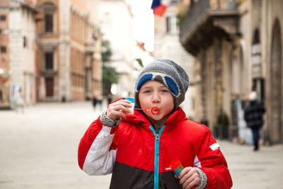 Portrait of playful boy wearing knit hat standing in city