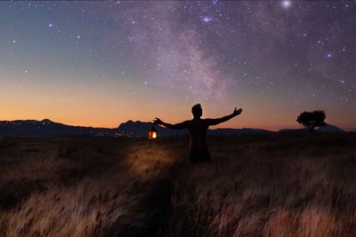 Rear view of man with arms outstretched standing against stars on field