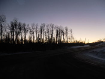 Bare trees on landscape at sunset