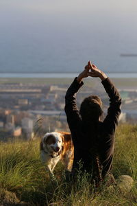 Rear view of woman doing yoga by dog on field