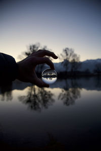 Reflection of hand holding water in lake against sky