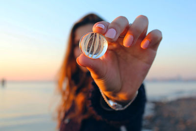 Woman holding marble at beach during sunset