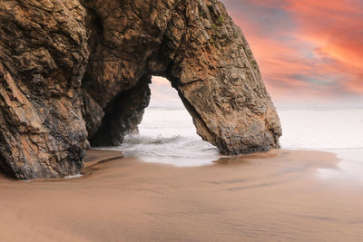 Rock formation on beach against sky during sunset