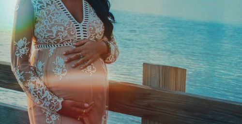 Midsection of pregnant woman standing by wooden railing