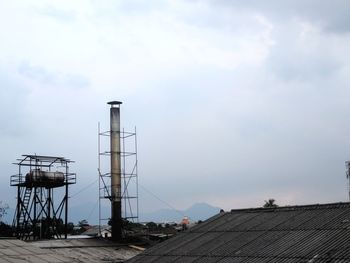 Electricity pylon by building against sky