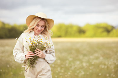 Smiling woman holding flowers on field