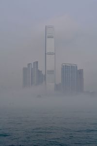 River with modern buildings in background against sky during foggy weather